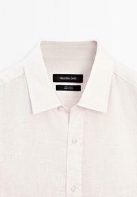 Light pink linen shirt with a classic collar, featuring a buttoned front and brand labels at the neck. Textured, breathable fabric.