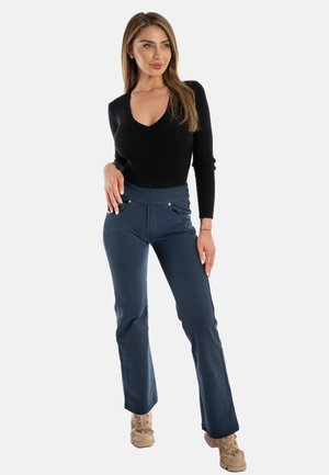 Maglia a maniche lunghe nera a coste abbinata a pantaloni blu aderenti, dotati di tasche con dettagli metallici e una finitura liscia e testurizzata.