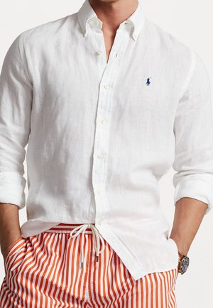 Homme portant une chemise blanche à boutons avec les manches retroussées et un pantalon rayé orange et blanc avec une taille à cordon.