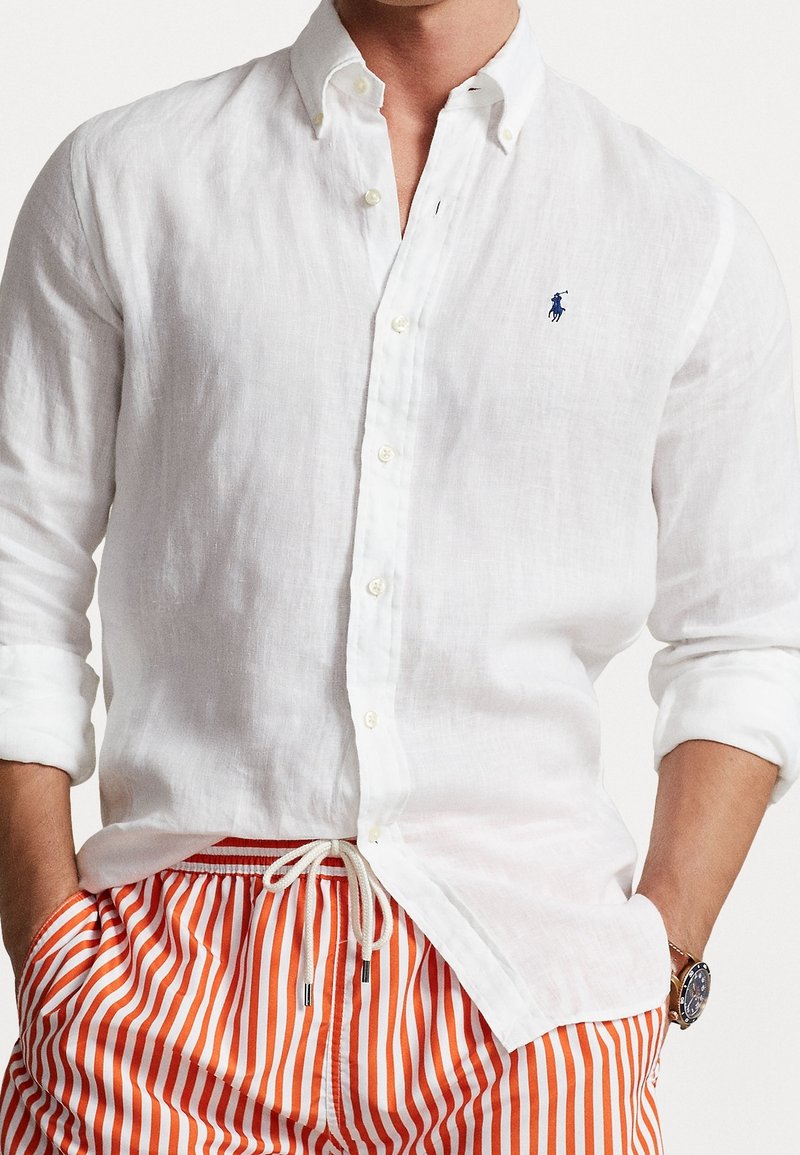 Homme portant une chemise blanche à boutons avec les manches retroussées et un pantalon rayé orange et blanc avec une taille à cordon.