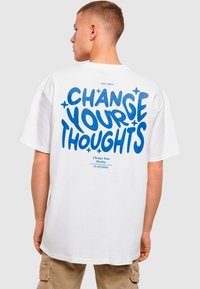 White cotton t-shirt featuring bold blue graphic text on the back that reads "CHANGE YOUR THOUGHTS" and smaller text below.