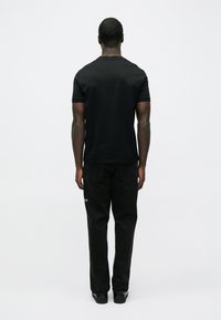 Musta puuvillainen lyhythihainen t-paita, yhdistettynä tummiin farkkuihin. Yksinkertainen muotoilu, ilman kuvioita tai näkyviä logoja, nähtynä takaa.