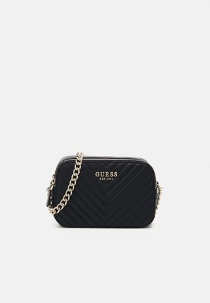 Schwarze gesteppte Guess Crossbody-Tasche mit goldener Kette als Trageriemen und Logo vorne, Reißverschluss oben vor weißem Hintergrund.