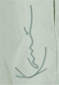 Lys grønn stoff med sølv broderi av abstrakte ansiktslinjer og kurver som skaper et minimalistisk design. Glatt tekstur.