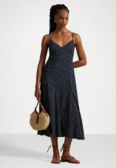 Navy floral dress with thin straps, a V-neck, and a flared hem. Worn with a round straw bag and strappy tan sandals.