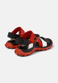 Röd och svart sandal med justerbara remmar, texturerad gummisula och vita detaljer. Har ett robust mönster för grepp.