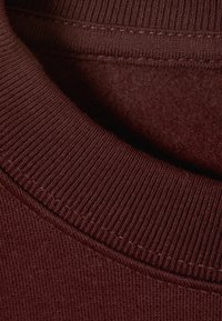 Burgunderfarbener Sweatshirt-Kragen mit Ripptextur, weicher Innenauskleidung und rundem Design mit präzisen Nähten entlang der Kanten.