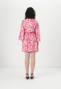 Abito floreale con motivi rosa, rossi e bianchi; maniche corte a campana; vita con cordoncino; orlo a ginocchio; abbinato a tacchi neri con cinturini.