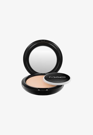 Miroir compact noir avec une poudre beige crémeuse à l'intérieur, accompagné d'un coussin applicateur rond. Design élégant avec une marque claire.