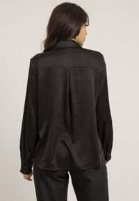 Chemise noire en satin avec un empiècement au dos et des poignets boutonnés. Caractéristiques d'un ourlet droit et d'une coupe décontractée, complétées par une texture lisse.