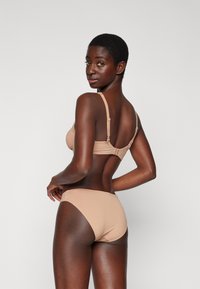 Ensemble de lingerie comprenant un soutien-gorge et un slip dans une teinte nude, fabriqué en tissu lisse. Le soutien-gorge est doté de bretelles réglables et d'une fermeture à crochet au dos.