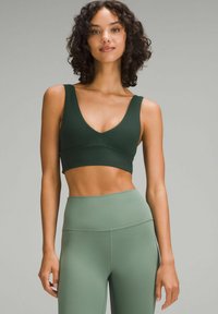 Grüner Sport-BH mit tiefem V-Ausschnitt und breiten Trägern, kombiniert mit hoch taillierten grünen Leggings. Glatte Stofftextur.