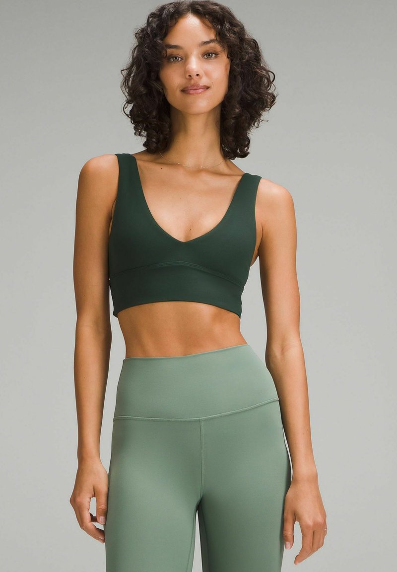 Grüner Sport-BH mit tiefem V-Ausschnitt und breiten Trägern, kombiniert mit hoch taillierten grünen Leggings. Glatte Stofftextur.