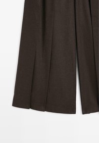 Pantalons marron à jambe large en tissu texturé, présentant des plis marqués et un ourlet net, conçus pour un ajustement sur mesure.