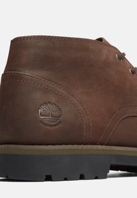 Stivaletto alla caviglia in pelle impermeabile marrone con forma rotonda, dettagli cuciti e logo. Suola in gomma con motivo antiscivolo.