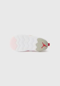 La suola delle scarpe Jordan presenta una base bianca con elementi rosa e grigi, una texture ondulata e un logo rosso sul tallone.