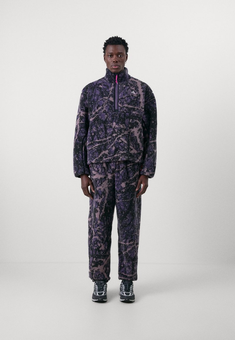 Fleece pullover and pants set in purple tones, featuring a zip collar, textured fabric, abstract pattern, and subtle brand logo on the chest.