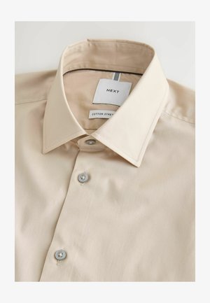 Beige bomulds knap-op skjorte med spids krave, mærket "NEXT" og "Cotton Street", pænt foldet mod en hvid baggrund.