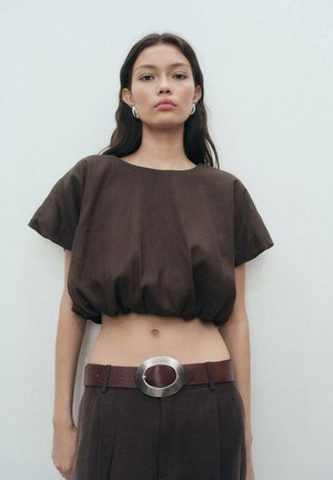Top corto marrón con un ajuste holgado, mangas cortas y un dobladillo elástico. Combinado con pantalones de tiro alto y un cinturón ancho con una hebilla ovalada de plata.