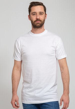 Witte katoenen t-shirt met korte mouwen en een ronde halslijn, gedragen door een persoon die tegen een effen achtergrond staat.