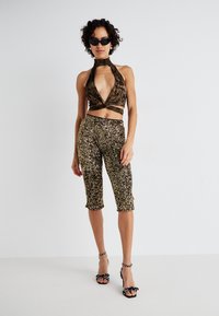 Haut à col halter avec un imprimé marron et noir, décolleté plongeant, associé à un pantalon en sequins dorés jusqu'aux genoux et des sandales à talons noires avec des nœuds.