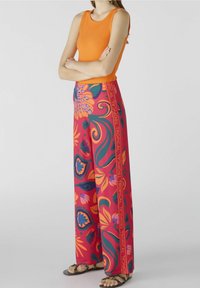 Débardeur orange à côtes associé à un pantalon large avec des motifs floraux et tropicaux vibrants en rose, vert et bleu. Sandales.