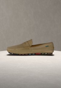 Mocassin en cuir beige avec détails cousus et semelle en caoutchouc multicolore, présenté sur un fond neutre.