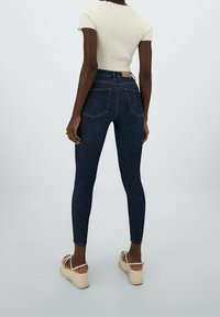 Jeans de mezclilla oscuros de tiro alto con cinco bolsillos y costuras en contraste, combinados con una camiseta blanca ajustada de canalé y sandalias de plataforma beige.