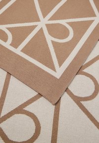 Dva overlappingové koberce s geometrickými vzormi v béžových a bielych odtieňoch, ukazujúce štruktúru a čisté okraje.