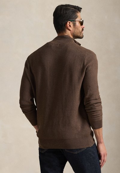 Rudas megztinis su apykakle, ribinėmis rankogaliais ir apačia. Dėvimas su tamsiais džinsais, matomas iš nugaros.