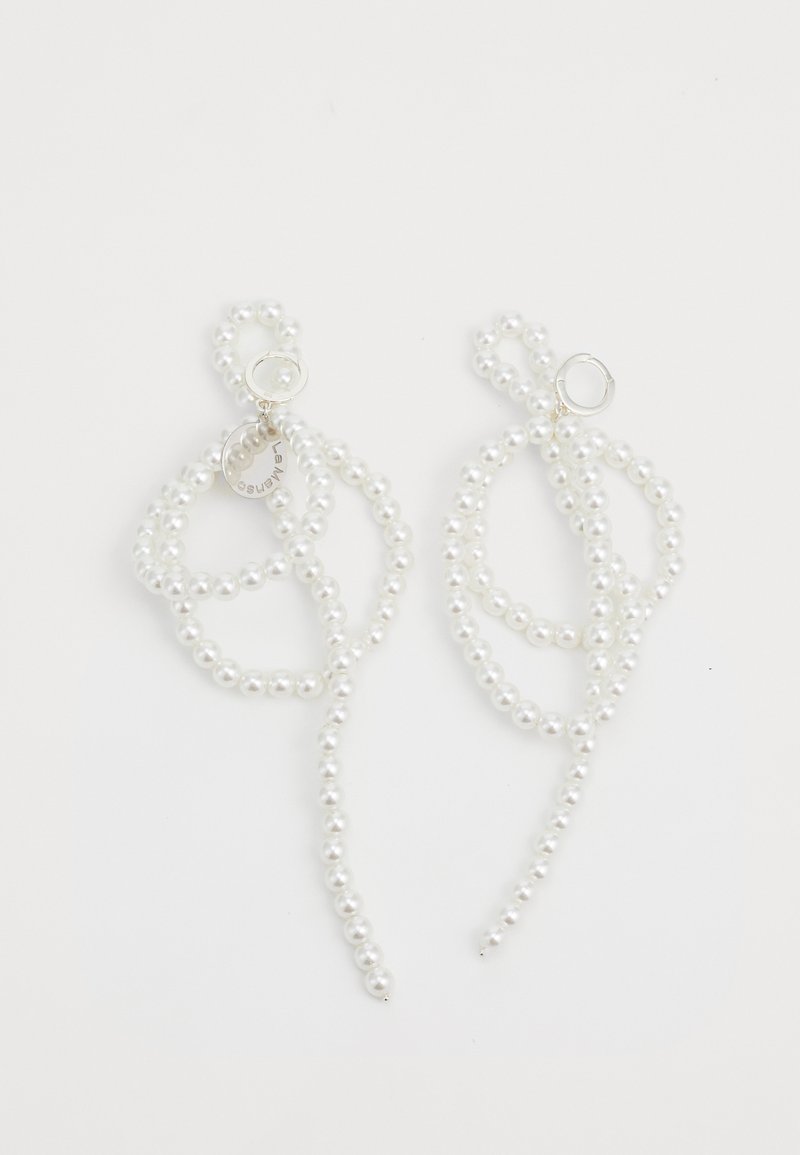 Balti perlų auskarai su sukamąja, pailga dizaino forma. Apima apvalų sidabro aksesuarą ir mažą etikėtę su prekės ženklu.