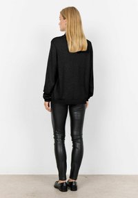 Zwarte oversized trui met lange mouwen, gecombineerd met slimfit zwarte leren leggings en zwarte schoenen. Gladde textuur, minimalistisch ontwerp.