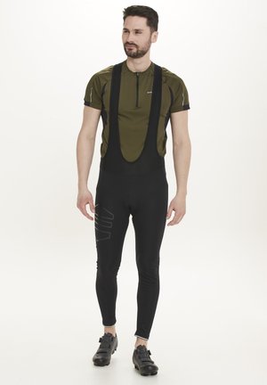Fietsoutfit met een groene short-sleeve top en zwarte bib tights, met grafische accenten. Het materiaal lijkt rekbaar en lichtgewicht.