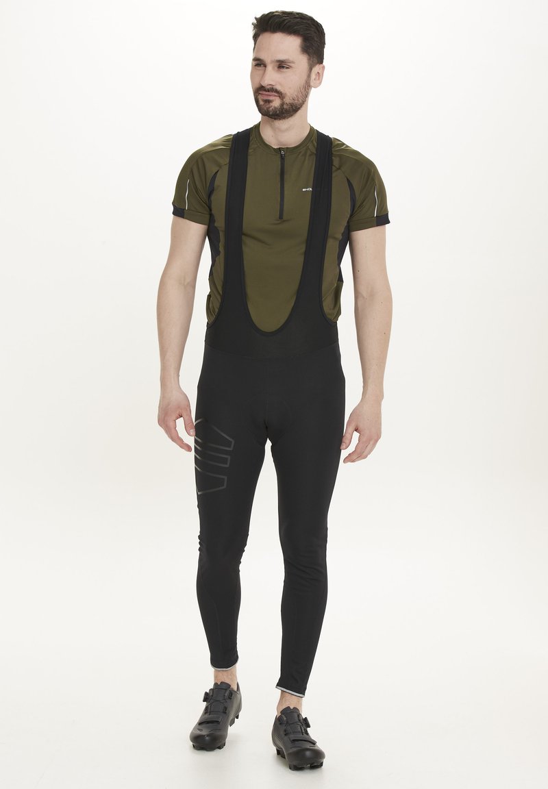 Cykeloutfit med en grön kortärmad topp och svarta bibbyxor, med grafiska detaljer. Materialet verkar stretchigt och lätt.