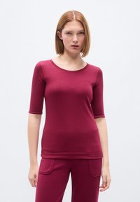 Μπορντό εφαρμοστό τοπ με μανίκια τριών τετάρτων, στρογγυλή λαιμόκοψη, λείο ύφασμα· συνδυασμένο με παντελόνι σε ίδιο χρώμα, με πλαϊνές τσέπες.