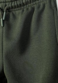 Tissu de pantalon de survêtement vert foncé avec une ceinture élastique et un cordon assorti visible en haut à gauche.