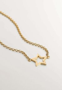 Collar de cadena de oro con un colgante en forma de estrella con un centro abierto. La cadena tiene eslabones entrelazados y una textura suave.