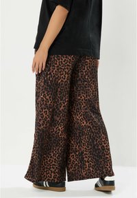Leopardenmuster weite Hose aus braunem und schwarzem Stoff, mit lockerer Passform und kombiniert mit schwarzen Sneakern.