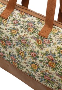 Sac fourre-tout avec design de tapisserie florale sur le tissu, base en cuir beige et poignées tressées marron. Présente des fleurs colorées et des accents feuillus.