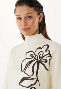 Maglione a collo alto di colore crema realizzato in tessuto morbido, caratterizzato da ricami floreali marrone scuro con petali e foglie ben evidenti.