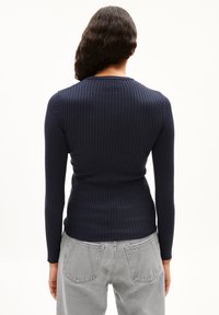 Marineblaues, geripptes Langarmoberteil mit taillierter Silhouette, rundem Halsausschnitt und subtiler Textur, kombiniert mit hellgrauen, hochgeschnittenen Jeans.