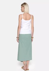 Lekki biały top na ramiączkach z cienkimi paskami, zestawiony z zwiewną, miętową maksisz skirt. Spódnica charakteryzuje się gładką teksturą i długością do kostek.