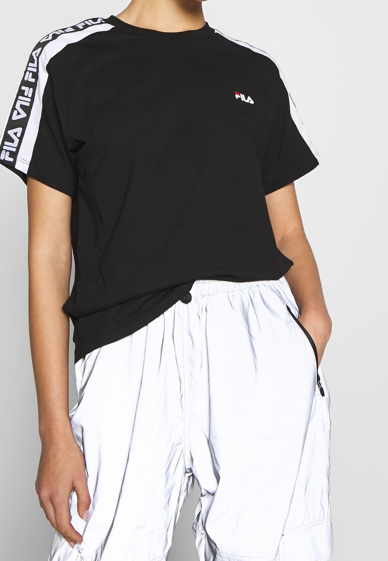 Svart bomullströja med vita sidosträck och Fila-logotyp. Kombinerad med ljusa, glänsande cargoshorts.