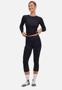 Black athletic long-sleeve top and capri leggings with textured accents, fitted design, and contrasting dark blue details. White and gray socks.