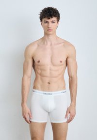Boxeri albi cu un design ajustat, curea elastică cu branding "Calvin Klein" și o textură netedă și elastică.