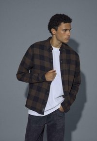 Bruin en zwart geruit overhemd met knopen over een wit T-shirt, met een klassieke kraag, ontworpen in zachte stof en een ontspannen pasvorm.
