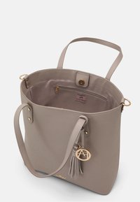 Krémová taška z umělé kůže s dvěma uchy, zlatavými kovovými prvky, odnímatelným třásněmi a vnitřní kapsou na zip.