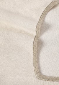 Svetlo kremna tkanina z mehko teksturo in ovalnim izrezom. Robovi so obrobljeni s kontrastnim kovinsko zlatim trakom, ki poudarja oblikovne detajle.