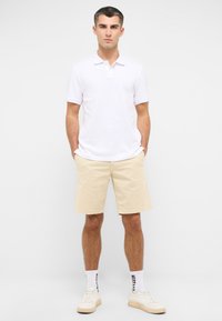 Chemise polo blanche associée à un short beige. L'ensemble présente un design classique avec une coupe confortable. Baskets et chaussettes mi-mollet incluses.