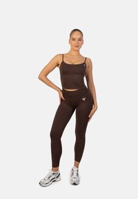Top corto deportivo marrón y leggings de cintura alta, hechos de material elástico, con un pequeño logo en la parte superior izquierda y en el lateral de la pierna.